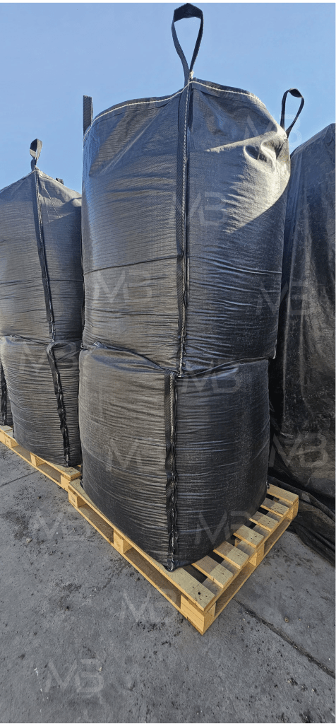 Bolsas grandes negras de almacenamiento apiladas sobre una plataforma de madera en un entorno industrial.